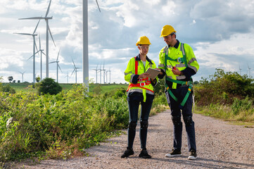 Two men in safety gear are standing on a road near a field of wind turbines