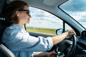 Young Caucasian woman in sunglasses driving a car in the countryside on a summer day - 779485615