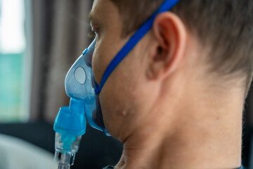Unhealthy man wearing nebulizer mask in home. Health, medical equipment and people concept - obrazy, fototapety, plakaty