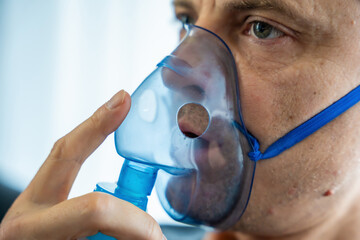 Close up view of unhealthy man wearing nebulizer mask in home. Health, medical equipment and people...