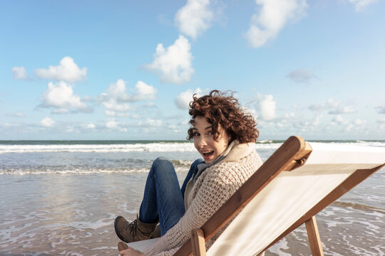 Cheerful woman sitting on deck chair looking back at beach