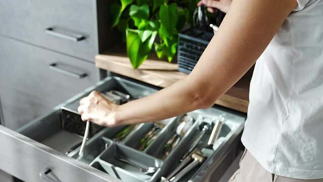 Housewife hands tidying up cutlery after dishwasher machine. Focus on woman neatly assembling fork, spoon, knife accessories for storage organization 