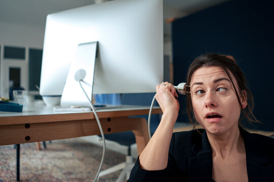 Overworked businesswoman holding electric plug by head at home office