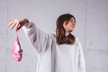 Girl holding deflated heart shaped pink balloon in front of gray concrete background