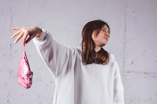 Girl holding deflated heart shaped pink balloon in front of gray concrete background