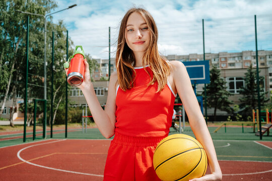 Teenage basketball player holding water bottle in school yard