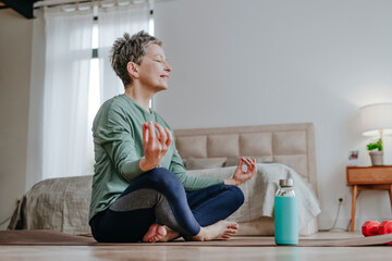 Smiling woman practicing yoga sitting on mat at home