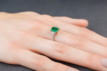 Beautiful female hand with gold ring with diamonds and emerald on gray background