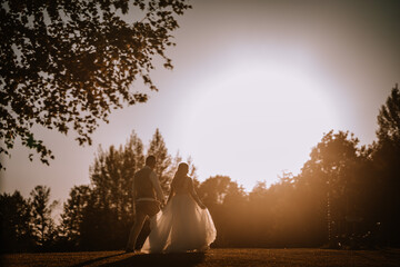 Valmiera, Latvia - August 13, 2023 - A backlit bride and groom hold hands and walk together, the...
