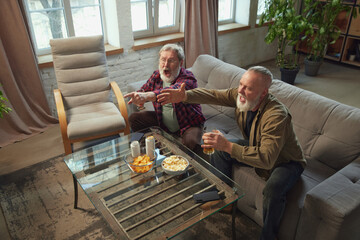Tense game moment. Two elderly men sitting in living room at home and emotionally watching online...
