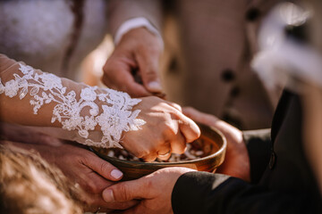 Valmiera, Latvia - Augist 13, 2023 - Hands reaching into a bowl, with one person wearing a lace sleeve, possibly during a wedding ceremony. - obrazy, fototapety, plakaty