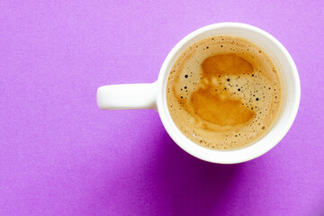 white cup of black espresso coffee on purple violet background, with a place for inscription, top view