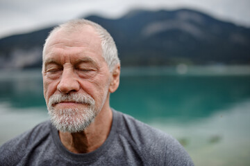 Portrait of active senior man resting after hiking in mountains. Thoughtful elderly man enjoying...