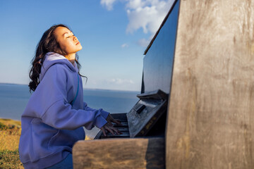 An attractive Asian woman has closed her eyes and is playing the piano outdoors.