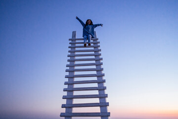 An attractive Asian woman is laughing and sitting at the top of a wooden staircase outdoors. A...