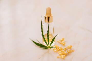 Mockup bottle of cosmetic product with cannabis leaves on beige background. Yellow capsules with whitening moisturizing facial serum with hyaluronic acid with hemp leaf on marble table.