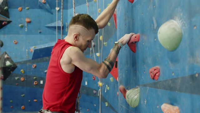 Sportsman with prothetic leg rubbing hands covered with chalk powder and climbing wall while practicing bouldering in indoor gym