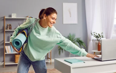  Positive woman with a sports bag, ready for training, turns off laptop on table, hurrying to leaving from home. She smiles, eager for gym session or outdoor workout, with fitness gear in bag. © Studio Romantic