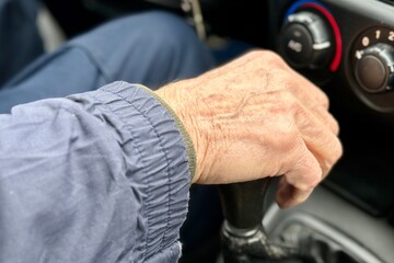 Close-up of an old wrinkled-skinned man's hand shifting gears on the lever of a car's manual...