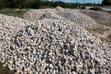 Em meio a um estaleiro na natureza, uma grande pilha de pequenos cubos de granito para o calcetamento de ruas ou passeios