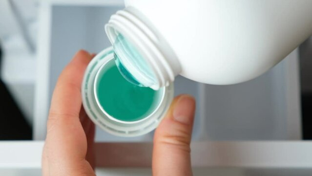 Liquid gel pouring into a lid against the background of an open tank of detergent washing machine