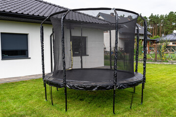 Large childrens jumping trampoline with protective net and closed zipper, standing in the garden.