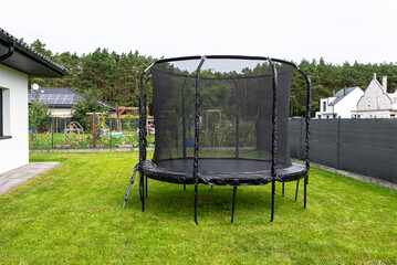 Large childrens jumping trampoline with protective net and closed zipper, standing in the garden, visible mesh masking the fence.