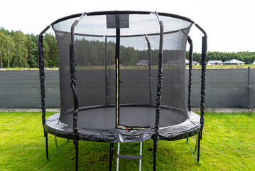 Large childrens jumping trampoline with protective net and closed zipper, standing in the garden, visible mesh masking the fence.