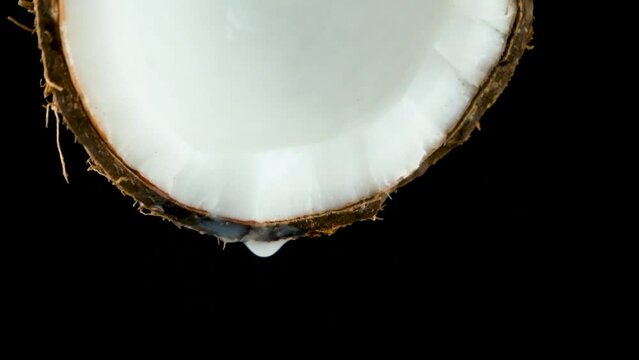Coconut water juice dripping from half of a coconut on black background slow motion.