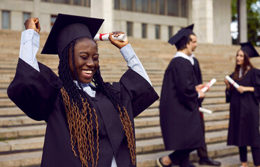 Young smiling excited african american student in a university gown and diploma in her hands. Happy...