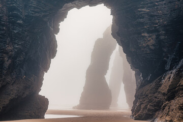 Playa de Las Catedrales in foggy day. Catedrais beach in Ribadeo, Lugo, Galicia, Spain. Natural archs of Cathedrals beach. Moody rock formations on misty day. Travel destination - 779530290