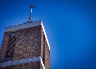 Das Foto zeigt die Spitze eines modernen Kirchturms einer evangelischen Kirche. Die klaren Linien und das zeitgenössische Design des Turms stehen im Kontrast zur traditionellen Architektur