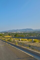 Vertical shot of asphalt road with barrier and townscape at a distance under blue sky