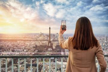 A tourist woman takes pictures with ther phone from the skyline of Paris, France, during sunset time - 779544208