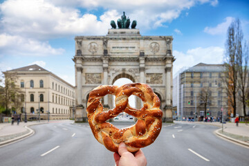 Munich travel concept with a hand holding a traditiona,l german Bretzel in front of the Victory Gate, Germany - 779544275