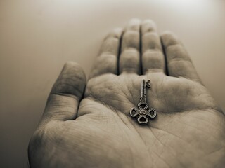 Closeup grayscale of a metal key in the palm of a person on an isolated background