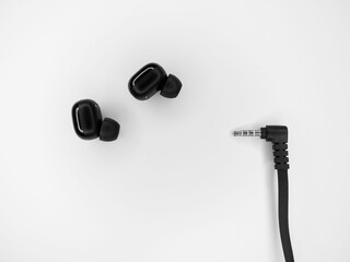 Top view grayscale of wireless earbuds and a wire of another device on a white background