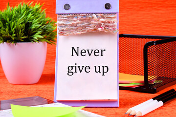 Never give up words It is written on a desktop calendar with loose leaves