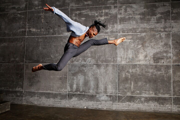 Energetic African American male dancer jumps in splits and stretching, twirls in a studio,...