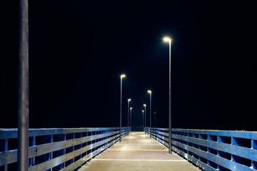 Lampposts along pier going into night darkness above sea symbolize serene scene of calmness cold...