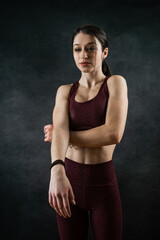 Young slim female fitness trainer wearing sports bra posign at studio isolated on black