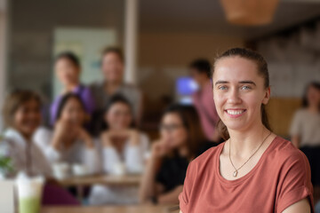 Young adult German woman sits in the middle of the cafe, soft focus, blurred people in cafe...