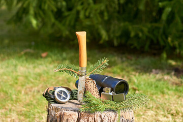 A rustic knife with a wooden handle, a vintage monocular, a lighter, a handheld compass, and a pine...