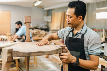 Carpenter working with electric planer on wooden plank in workshop. Craftsman makes own successful small business, Asian man using tool in carpenter's shop to making a furniture from wood - obrazy, fototapety, plakaty