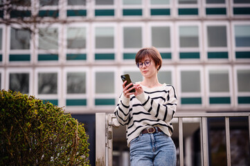 Fototapeta premium In an elegant blend of city vibes and personal time, a woman captures herself with her smartphone, standing before a geometrically patterned building facade.