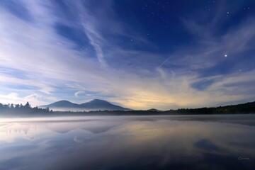 Silhouette view of the trees around a lake in the forest with mountains in the background