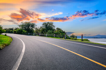 Asphalt highway road and green trees with colorful sky clouds at dusk