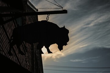 Silhouette of a buffalo sign hanging on a building outdoors against blue sky