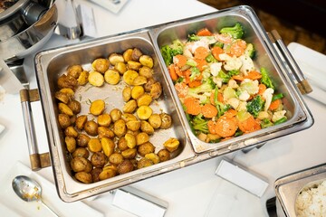 High-angle shot of pans full of baked potatoes and a salad with carrot, broccoli and beans