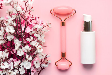 Closeup of jade massanger roller, facial cream bottle for skin care and almond blossoms. Skin care products concept